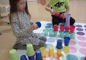 Nel i Konrad układają wieżę z kolorowych kubeczków zgodnie z instrukcją